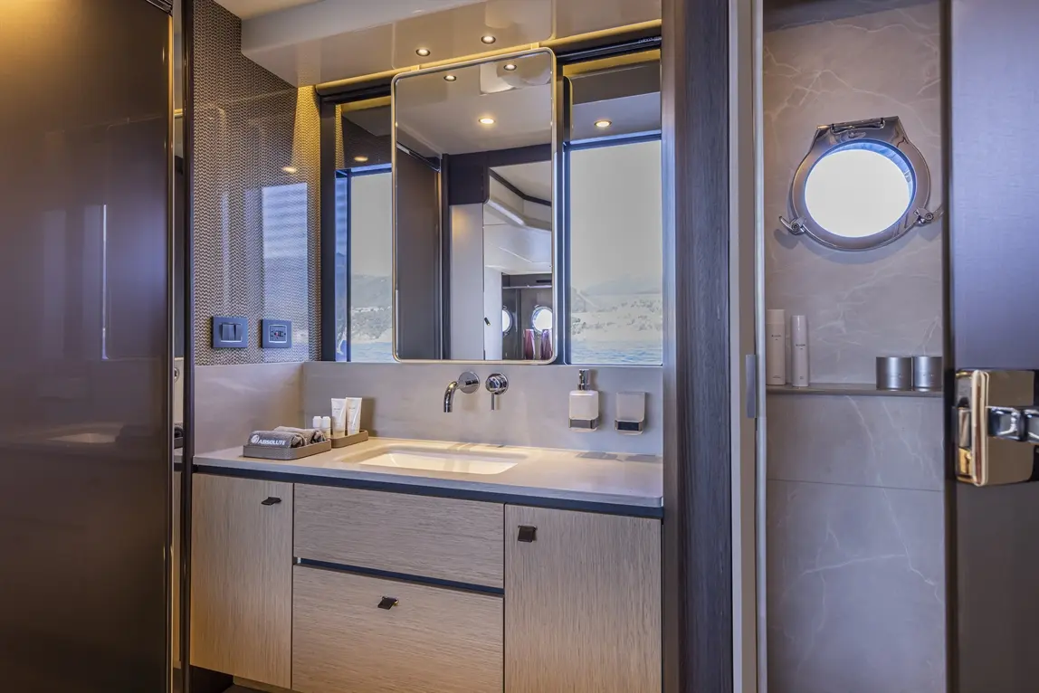 Luxurious bathroom with modern fixtures, a large mirror, and a sea view through a round window, showcasing premium toiletries.